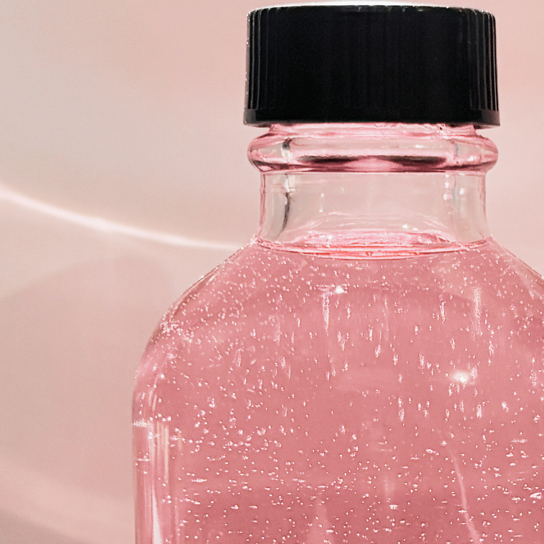 Pink Rosehip seed oil bubbles in a glass bottle soft pink background